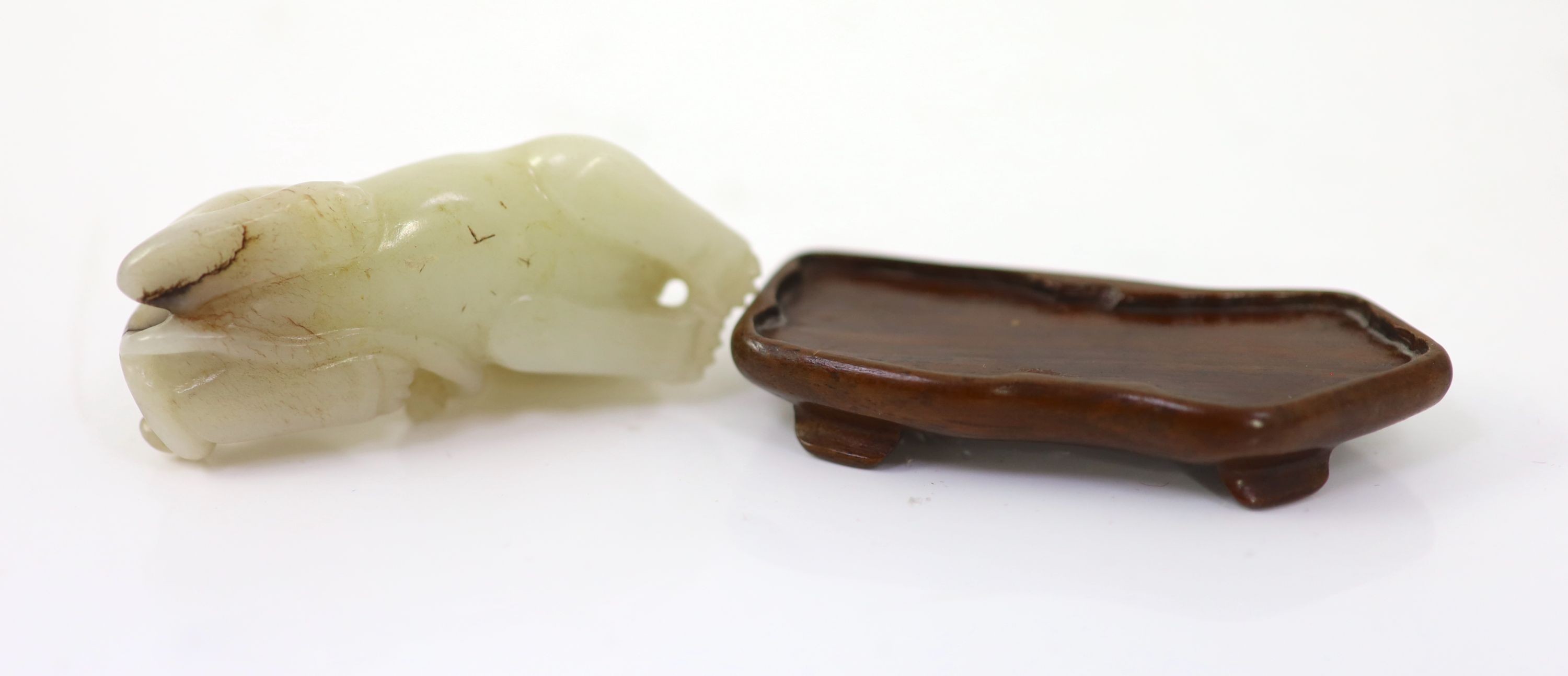 A Chinese pale celadon and brown jade figure of a lion-dog, 18th/19th century, 6.7cm long, wood stand